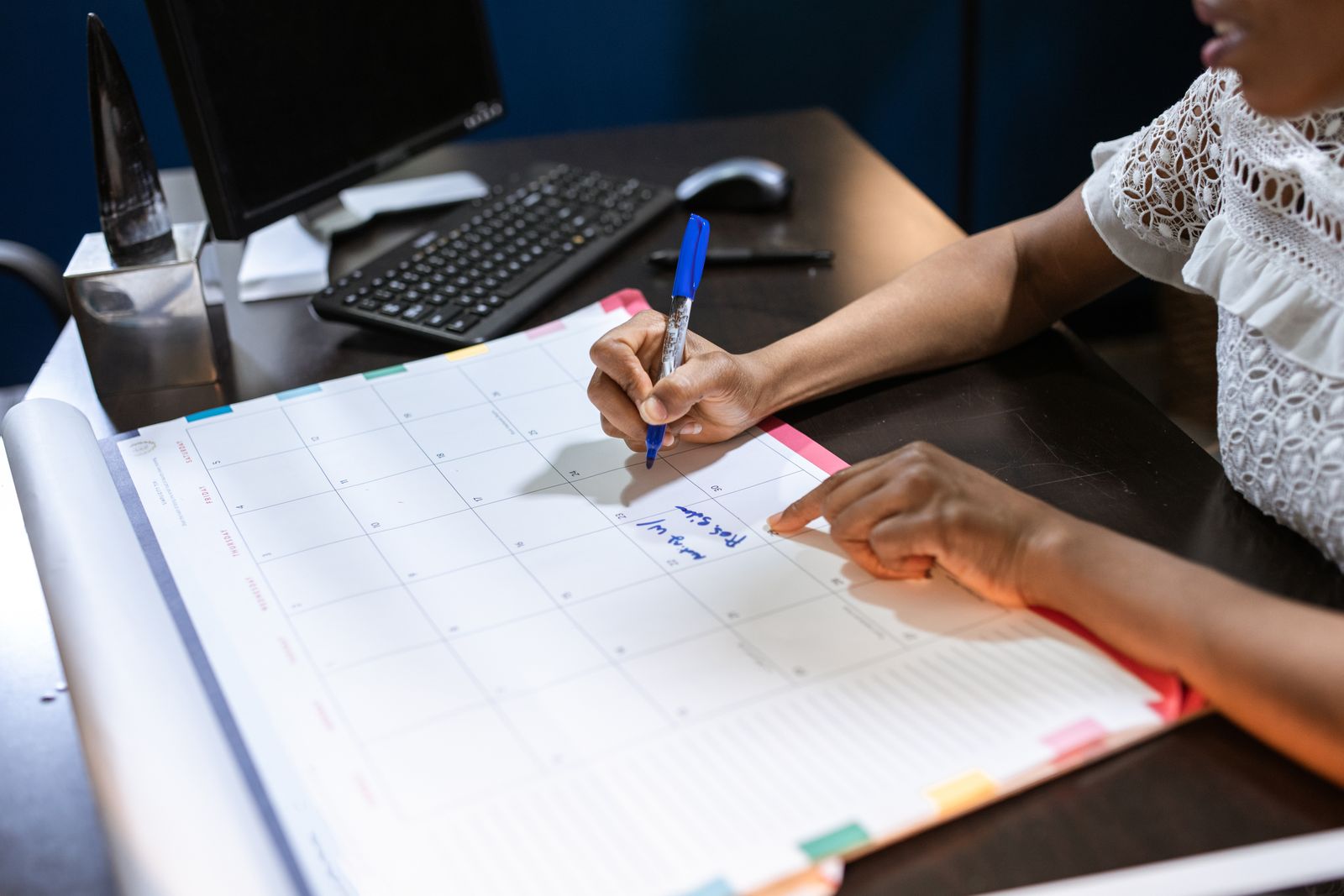 Marcar direto na agenda central, não numa anotação solta, é o que evita o conflito depois Pessoa marcando um compromisso com caneta num planner de mesa, ao lado do computador