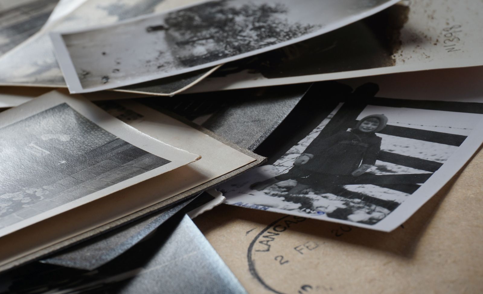 Pilha de fotografias antigas em preto e branco, algumas desgastadas pelo tempo, sobre uma superfície de papel
