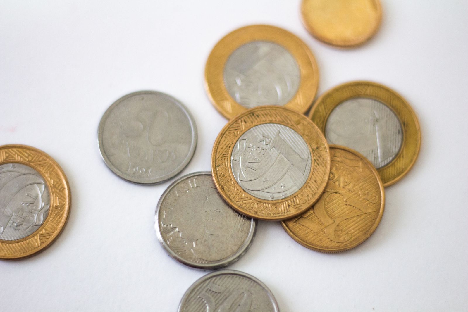 O começo costuma ser assim: pouco volume, preço em descoberta, troco contado Moedas de real brasileiro espalhadas sobre uma superfície branca, incluindo uma moeda antiga de 50 centavos