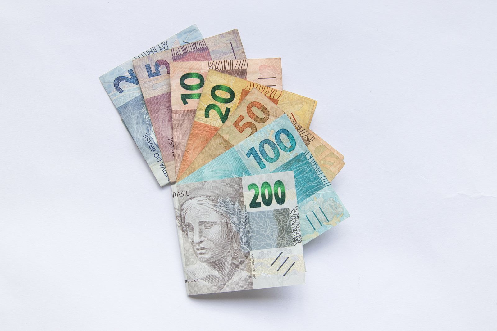 Notas de real brasileiro de várias cédulas, de 2 a 200 reais, abertas em leque sobre fundo branco